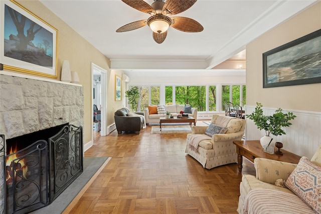 90 Shingle House Rd, Millwood, NY 10546 - living room featuring a stone fireplace, a ceiling fan, baseboard heating, a wainscoted wall, and ornamental molding