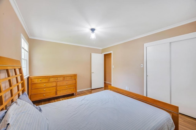 bedroom with wood finished floors, ornamental molding, a closet, and baseboards