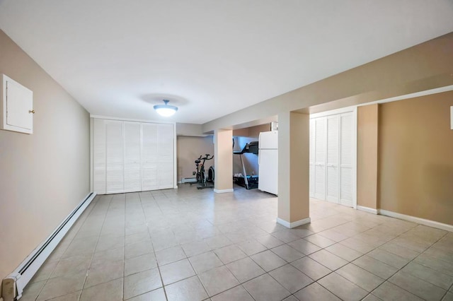 finished below grade area with freestanding refrigerator, baseboard heating, light tile patterned flooring, baseboards, and a baseboard radiator
