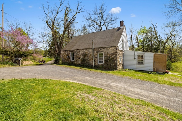 view of side of home featuring a chimney, stone siding, dirt driveway, and a lawn