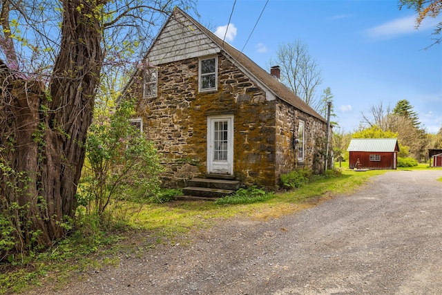 exterior space with stone siding, dirt driveway, a chimney, and entry steps