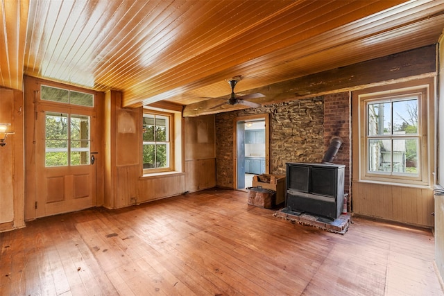 unfurnished room with wood ceiling, wood-type flooring, ceiling fan, a wood stove, and wooden walls