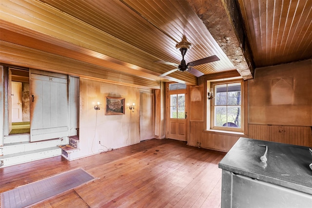 interior space featuring wood walls, hardwood / wood-style floors, wooden ceiling, beamed ceiling, and a ceiling fan