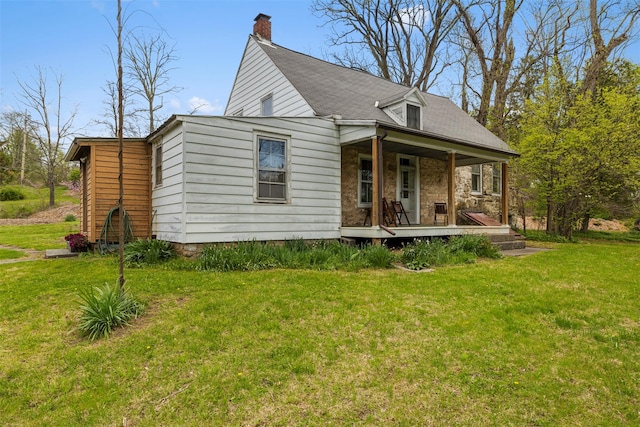 rear view of property with covered porch, a chimney, and a lawn
