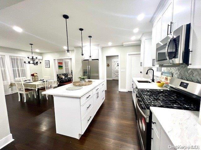 2906 Oceanside Rd, Oceanside, NY 11572 - kitchen featuring stainless steel appliances, a sink, dark wood finished floors, white cabinets, and a chandelier