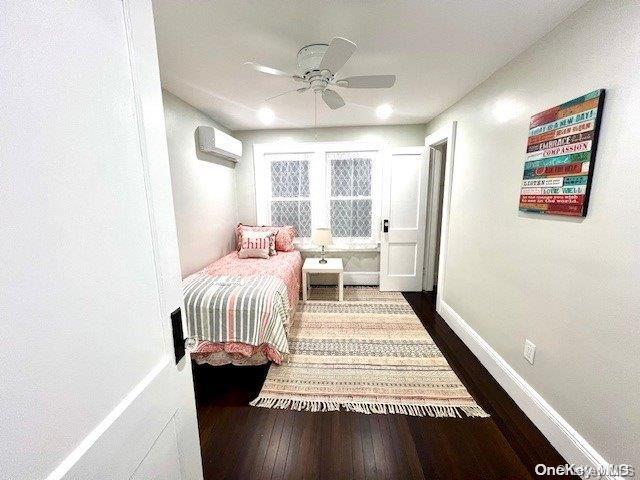2906 Oceanside Rd, Oceanside, NY 11572 - bedroom featuring dark wood-type flooring, a wall unit AC, baseboards, and ceiling fan