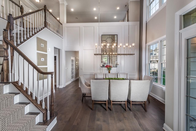 dining room with a towering ceiling, plenty of natural light, stairs, wood finished floors, and baseboards