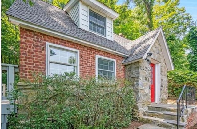 exterior space featuring brick siding and roof with shingles