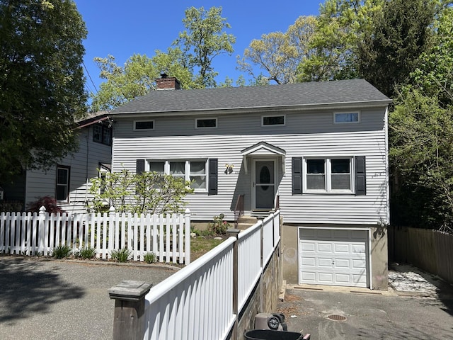 view of front of house featuring a chimney, a fenced front yard, a garage, and aphalt driveway
