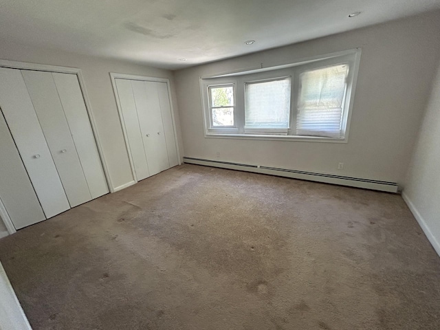 unfurnished bedroom featuring a baseboard heating unit, baseboards, multiple closets, and carpet floors