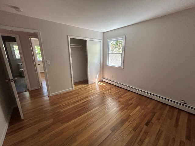 unfurnished bedroom featuring a closet, wood finished floors, baseboards, and a baseboard heating unit