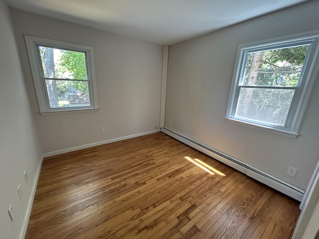 spare room with baseboards, baseboard heating, plenty of natural light, and wood finished floors