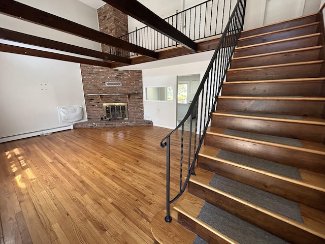 stairs featuring a fireplace, a high ceiling, baseboard heating, and wood finished floors