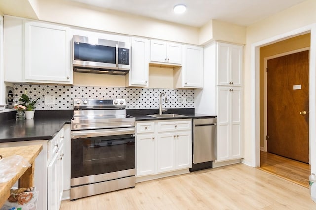 kitchen featuring a sink, stainless steel appliances, light wood finished floors, backsplash, and white cabinets