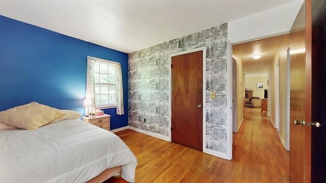 bedroom with baseboards, wallpapered walls, an accent wall, and wood finished floors