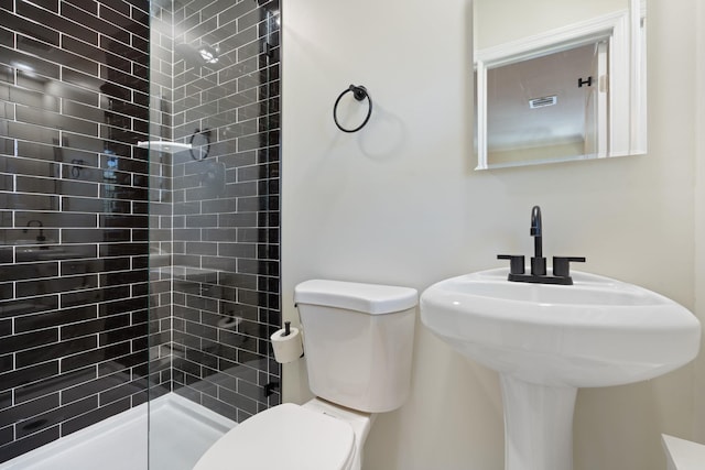 full bathroom with toilet, visible vents, tiled shower, and a sink