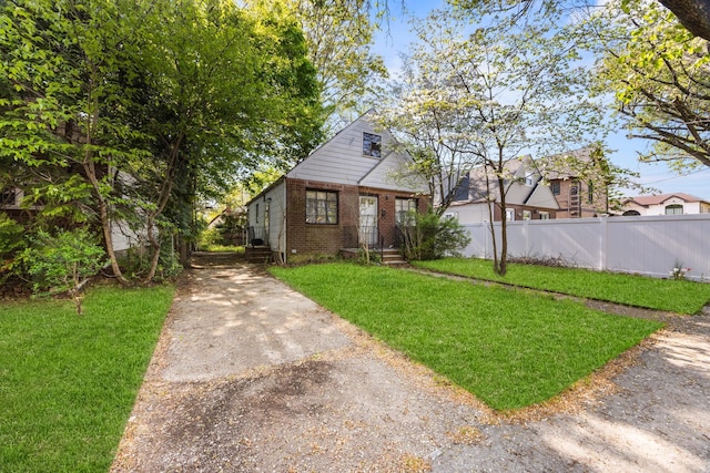 bungalow-style house featuring fence, a front lawn, brick siding, and driveway