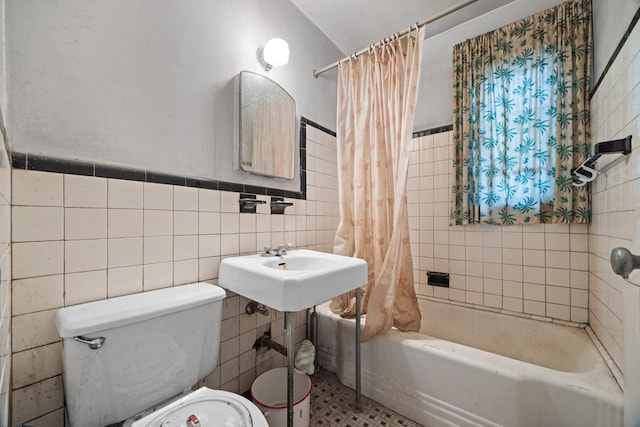 full bath featuring tile walls, toilet, shower / bath combination with curtain, a sink, and a wainscoted wall