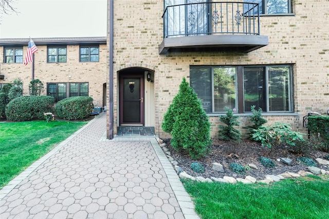 view of exterior entry featuring brick siding and a balcony