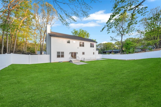 rear view of house with a fenced backyard, a chimney, and a lawn