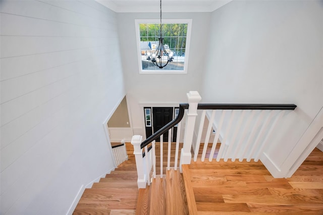 stairway with baseboards, a notable chandelier, crown molding, and wood finished floors