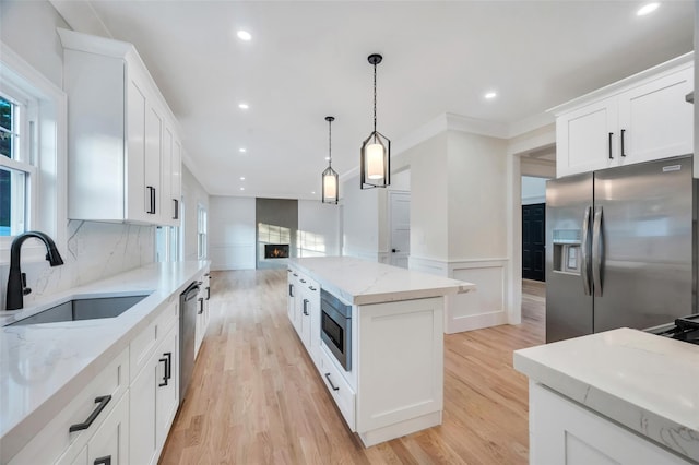 kitchen with light wood finished floors, a sink, a lit fireplace, appliances with stainless steel finishes, and a kitchen island