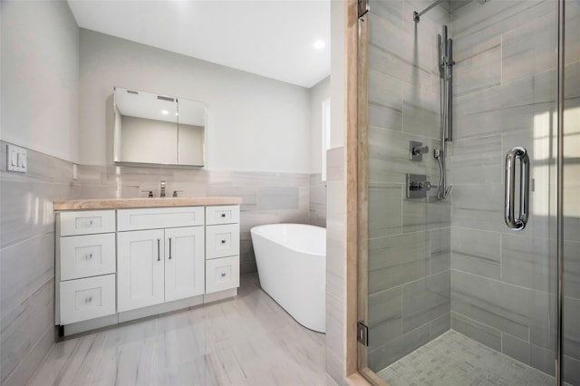bathroom with a wainscoted wall, tile walls, a freestanding bath, a shower stall, and vanity