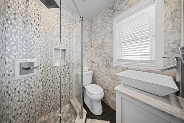 bathroom featuring toilet, a stall shower, tile patterned flooring, vanity, and tile walls