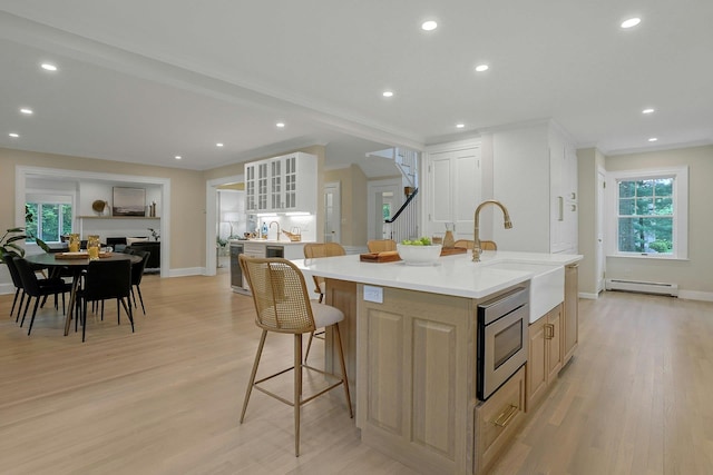 490 Bellwood Ave, Sleepy Hollow, NY 10591 - kitchen with stainless steel microwave, a sink, a center island with sink, baseboard heating, and light wood-style flooring