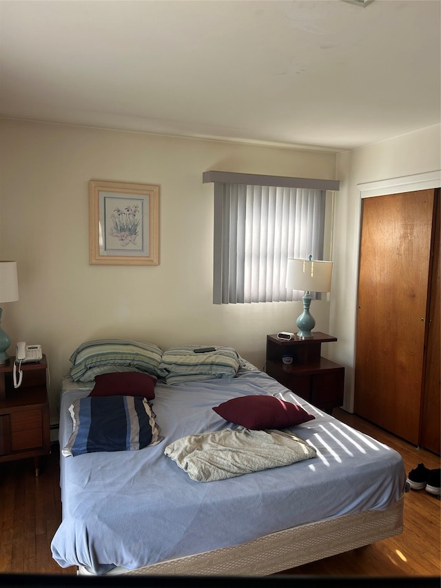 bedroom with a closet, hardwood / wood-style floors, and baseboard heating
