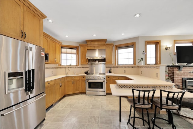 kitchen featuring stainless steel appliances, a peninsula, wall chimney exhaust hood, and plenty of natural light