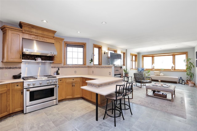 kitchen with light countertops, stainless steel range with gas stovetop, backsplash, wall chimney range hood, and recessed lighting