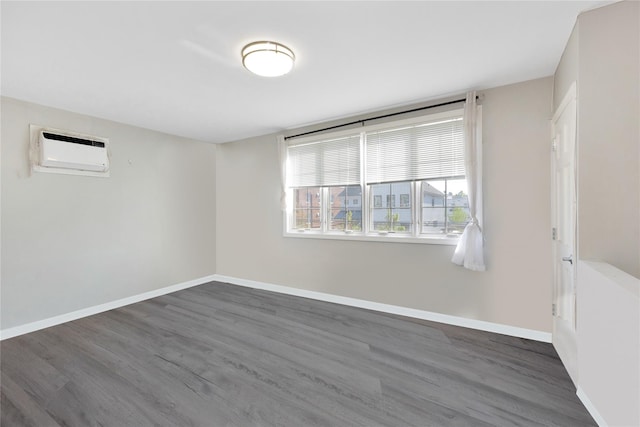 spare room featuring a wall mounted AC, baseboards, and wood finished floors