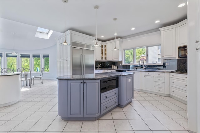 kitchen featuring built in fridge, black microwave, a warming drawer, a skylight, and tasteful backsplash
