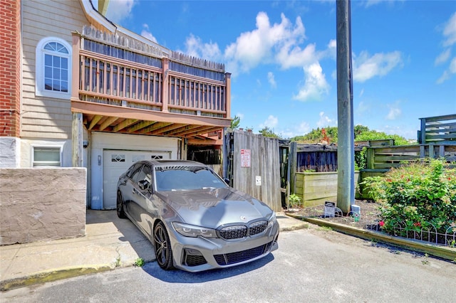 exterior space with a balcony, aphalt driveway, an attached garage, and fence