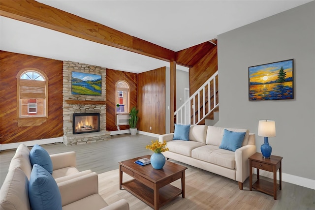 living area with baseboards, a stone fireplace, stairs, wooden walls, and wood finished floors