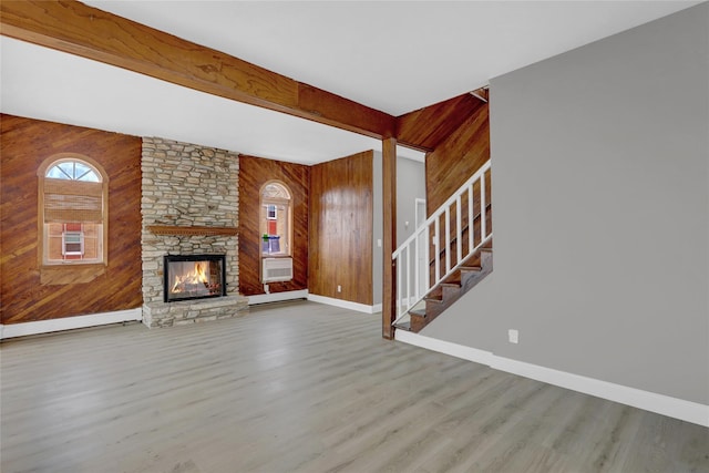 unfurnished living room with wood finished floors, wood walls, baseboards, a stone fireplace, and stairs