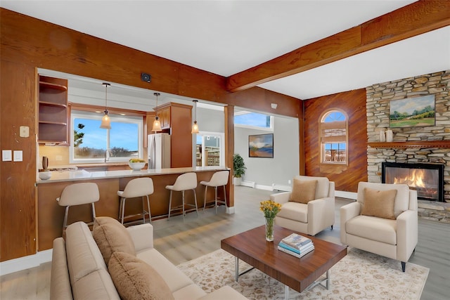 living area featuring baseboards, a wealth of natural light, beam ceiling, and light wood-type flooring