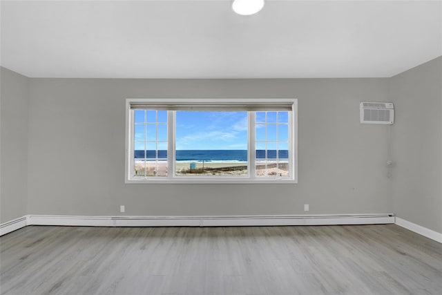 spare room featuring a water view, wood finished floors, baseboards, baseboard heating, and a wall mounted AC