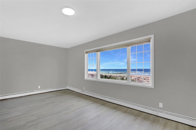 empty room featuring baseboards, baseboard heating, a water view, and wood finished floors