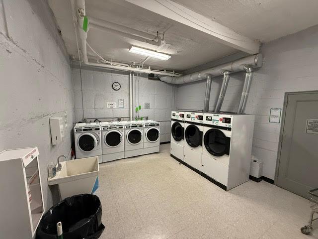 community laundry room featuring tile patterned floors, independent washer and dryer, concrete block wall, and a sink