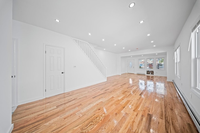 unfurnished living room featuring a baseboard heating unit, stairway, recessed lighting, and light wood-style floors
