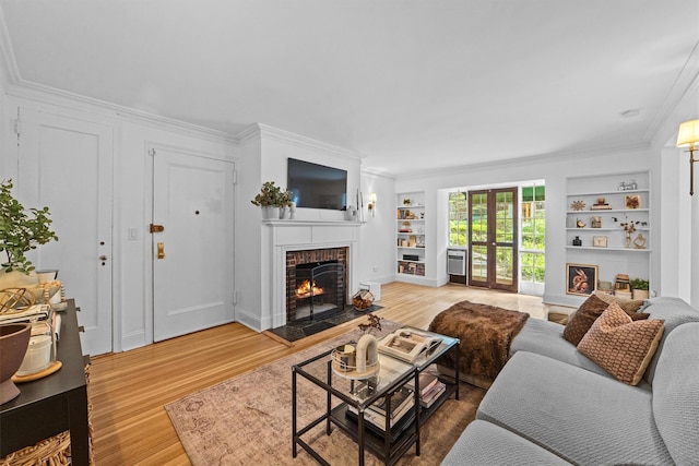 living area with built in features, a fireplace, wood finished floors, and ornamental molding