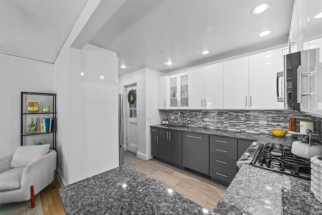 kitchen featuring white cabinetry, dark stone counters, backsplash, a sink, and recessed lighting