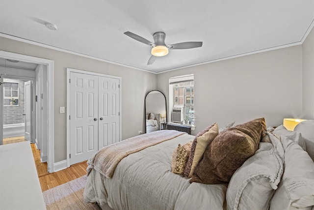 bedroom featuring crown molding, a closet, baseboards, light wood finished floors, and radiator heating unit