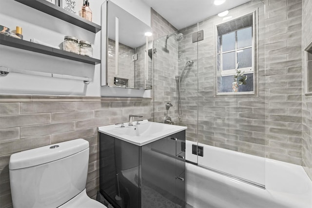 bathroom with combined bath / shower with glass door, toilet, vanity, and tile walls