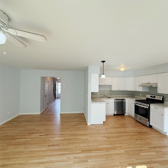 kitchen featuring under cabinet range hood, stainless steel appliances, tasteful backsplash, and light countertops