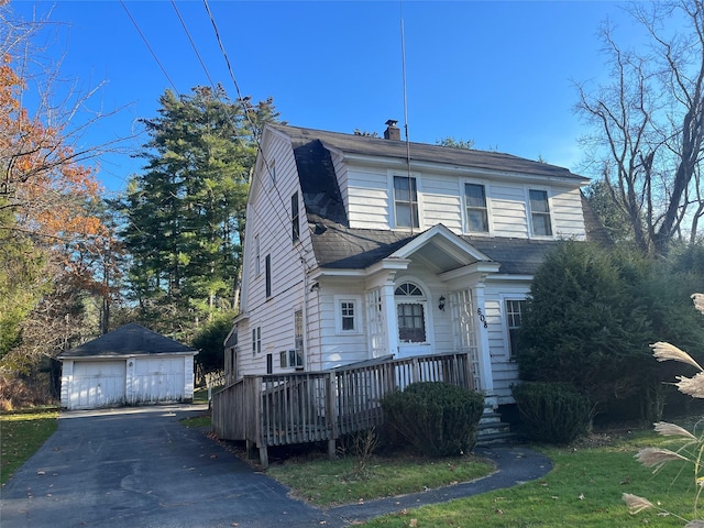 view of front facade featuring a chimney, a gambrel roof, an outdoor structure, a detached garage, and a deck