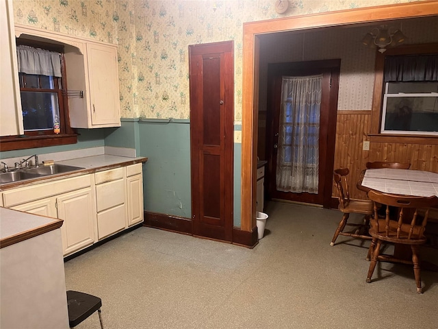kitchen with a sink, wallpapered walls, a wainscoted wall, light countertops, and wooden walls