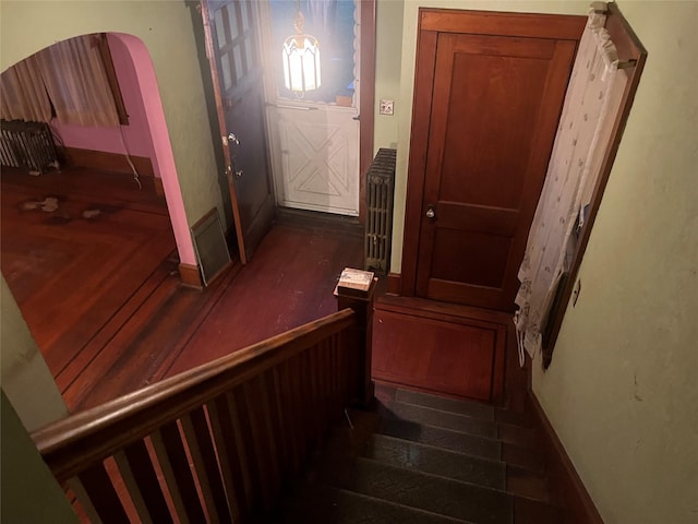 staircase featuring baseboards, radiator heating unit, and arched walkways